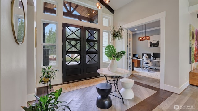 entryway with wood finished floors, baseboards, beam ceiling, french doors, and a towering ceiling
