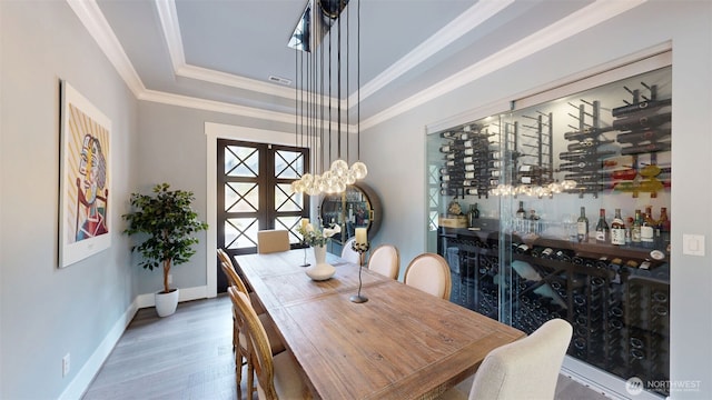 dining space featuring wood finished floors, visible vents, baseboards, a tray ceiling, and ornamental molding