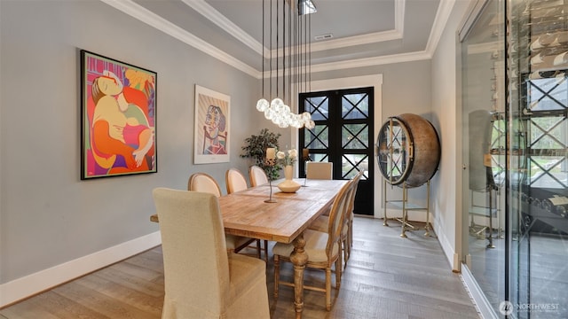 dining space with a tray ceiling, baseboards, crown molding, and hardwood / wood-style flooring