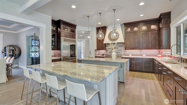 kitchen with light wood-style flooring, an island with sink, built in fridge, and a sink