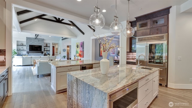 kitchen with stainless steel microwave, light wood-style flooring, a kitchen island with sink, and beam ceiling
