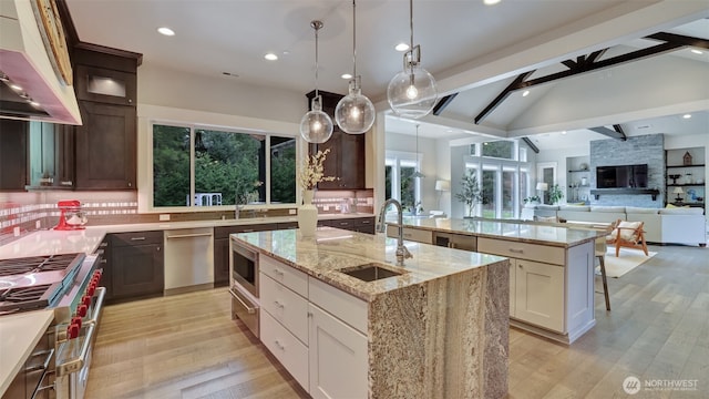 kitchen featuring light wood-type flooring, an island with sink, a sink, backsplash, and vaulted ceiling with beams