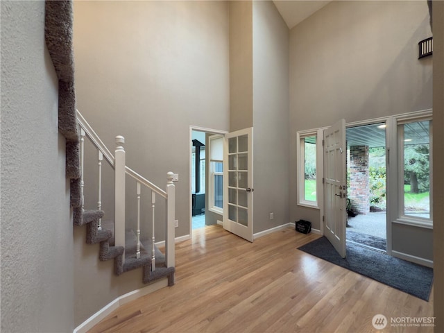 foyer entrance with baseboards, wood finished floors, french doors, and stairway