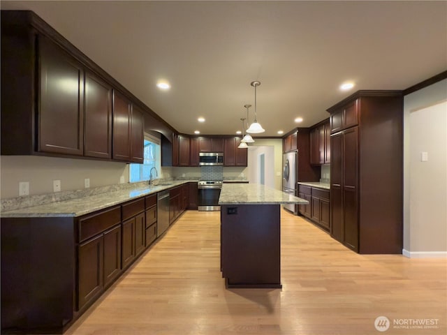 kitchen with light stone counters, a sink, appliances with stainless steel finishes, a center island, and light wood-style floors
