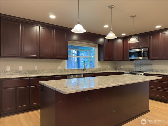kitchen with a center island, light wood-style floors, light stone countertops, dark brown cabinets, and appliances with stainless steel finishes