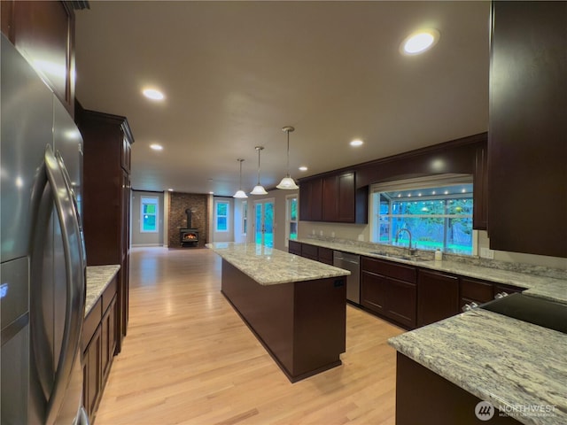 kitchen featuring a sink, a kitchen island, a wood stove, light wood-type flooring, and stainless steel appliances