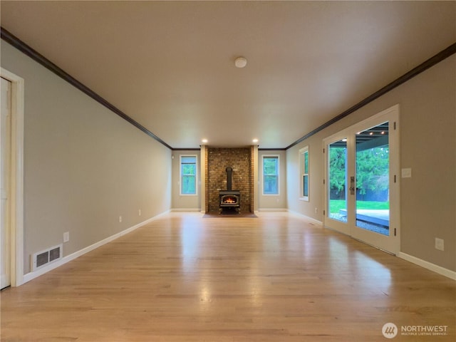 unfurnished living room with a wood stove, ornamental molding, baseboards, light wood-style floors, and visible vents