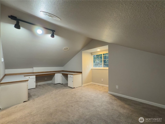 additional living space featuring carpet flooring, built in desk, lofted ceiling, and a textured ceiling