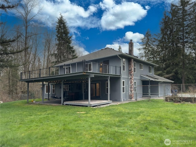 rear view of house featuring a chimney, a deck, fence, and a yard
