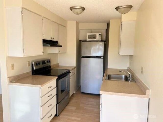 1930 Lawrence St Unit 21, Port Townsend, WA 98368 - kitchen featuring stainless steel appliances, under cabinet range hood, a sink, light wood-style floors, and white cabinets