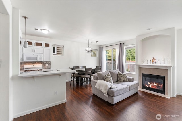 living room with a tiled fireplace, dark wood-style flooring, baseboards, and a notable chandelier