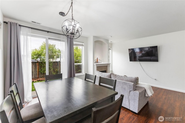 dining space featuring dark wood-style flooring, a notable chandelier, a fireplace, baseboards, and visible vents