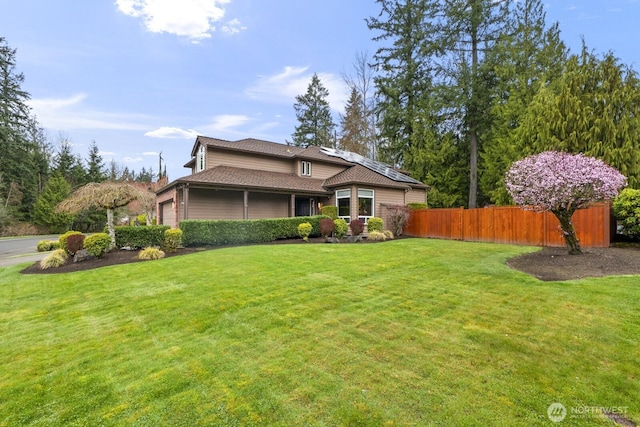 view of front of property with fence, an attached garage, a front lawn, and roof mounted solar panels