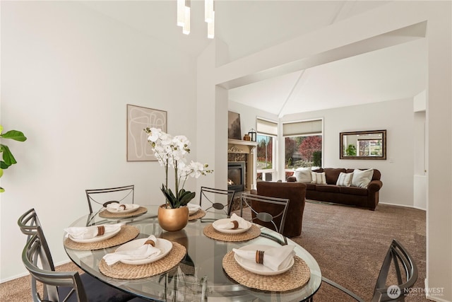 carpeted dining area with vaulted ceiling and a glass covered fireplace