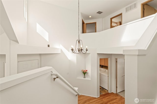 stairway with separate washer and dryer, wood finished floors, visible vents, and a chandelier