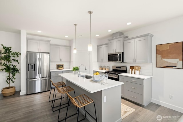 kitchen with gray cabinets, a sink, appliances with stainless steel finishes, a center island with sink, and light wood-type flooring