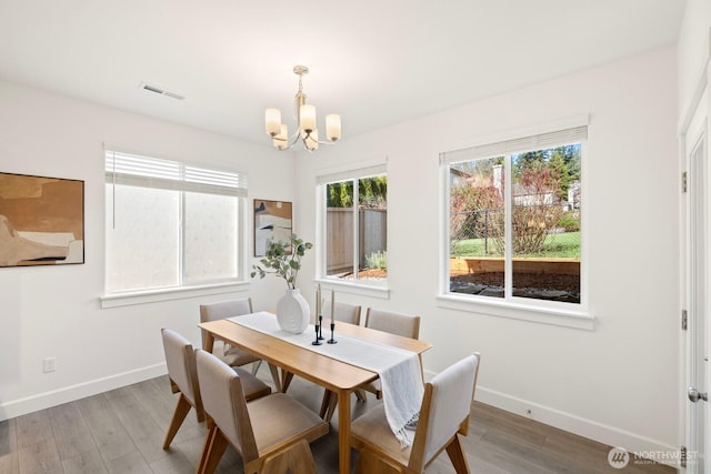 dining space featuring baseboards, light wood-style flooring, visible vents, and a notable chandelier