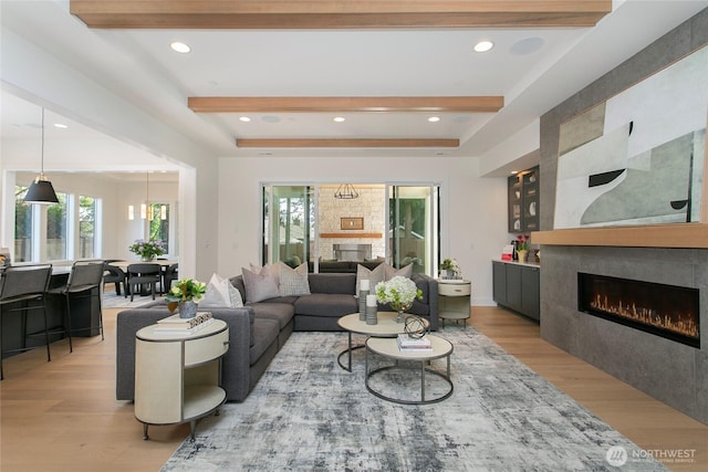 living room featuring plenty of natural light, light wood-style flooring, beamed ceiling, and a large fireplace