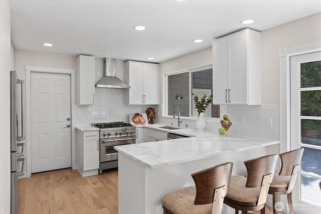 1825 112th Ave NE, Bellevue, WA 98004 - kitchen with wall chimney range hood, a peninsula, light wood-style flooring, appliances with stainless steel finishes, and a sink
