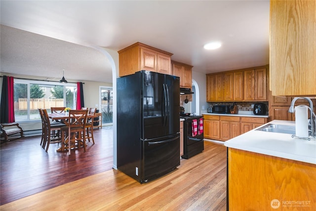 kitchen featuring light wood-style floors, arched walkways, black appliances, under cabinet range hood, and a sink