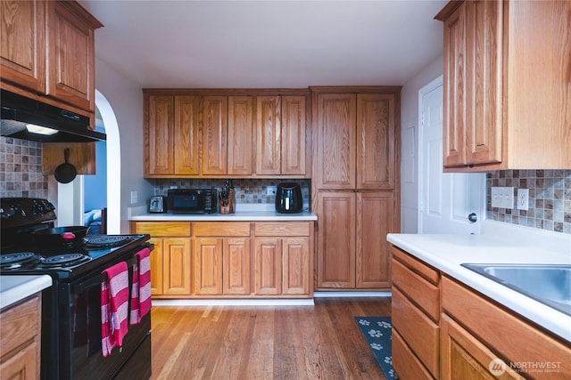 kitchen featuring under cabinet range hood, light countertops, black electric range oven, brown cabinets, and light wood finished floors