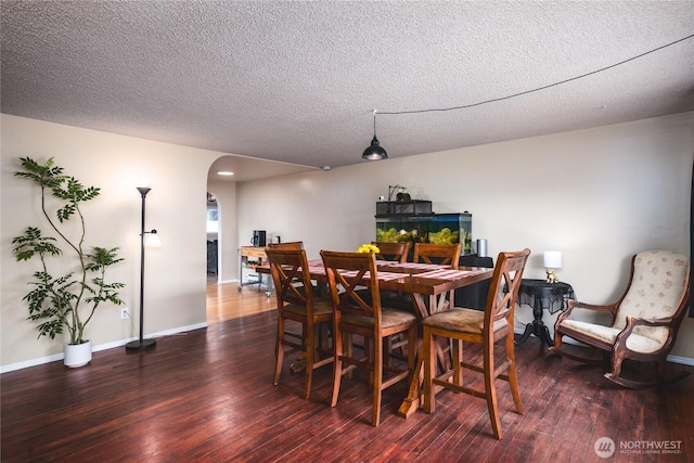 dining area with baseboards, arched walkways, wood finished floors, and a textured ceiling