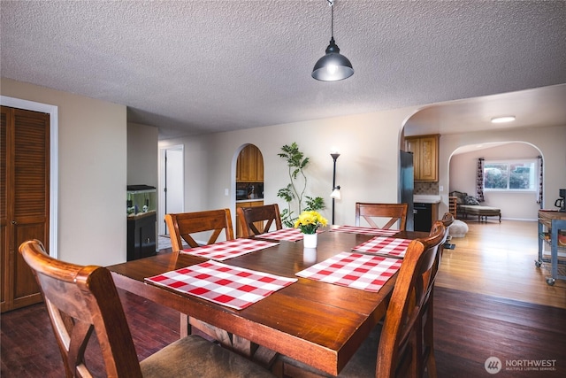 dining area featuring arched walkways, wood finished floors, and a textured ceiling