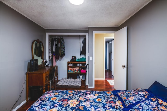 bedroom with a closet, baseboards, a textured ceiling, crown molding, and wood finished floors