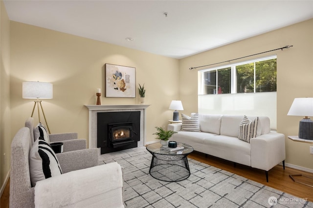 living area with baseboards, a glass covered fireplace, and wood finished floors