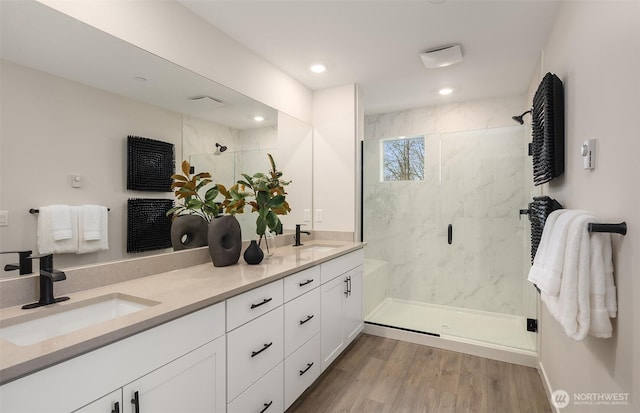 full bath featuring double vanity, wood finished floors, a marble finish shower, and a sink