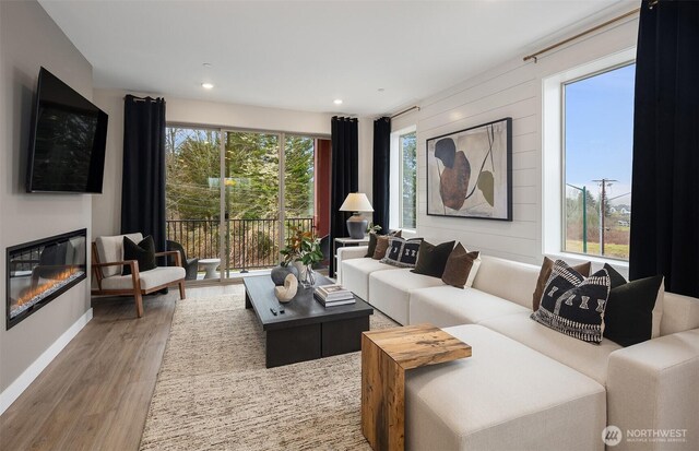 living area featuring a glass covered fireplace, recessed lighting, baseboards, and wood finished floors