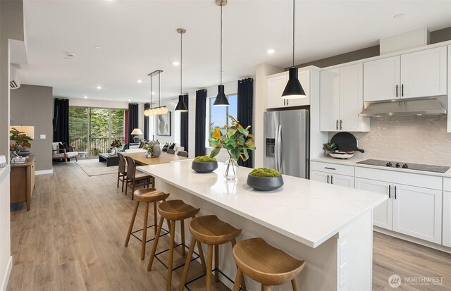 kitchen featuring light wood finished floors, tasteful backsplash, black electric stovetop, under cabinet range hood, and stainless steel refrigerator with ice dispenser