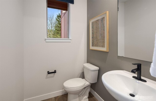 half bathroom featuring a sink, baseboards, toilet, and wood finished floors