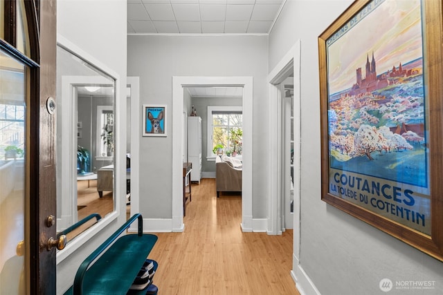 corridor featuring ornamental molding, baseboards, and light wood finished floors