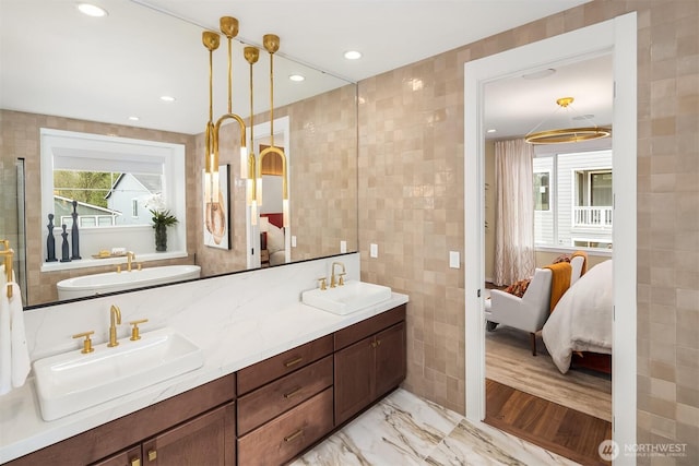 ensuite bathroom featuring tile walls, recessed lighting, marble finish floor, and a sink