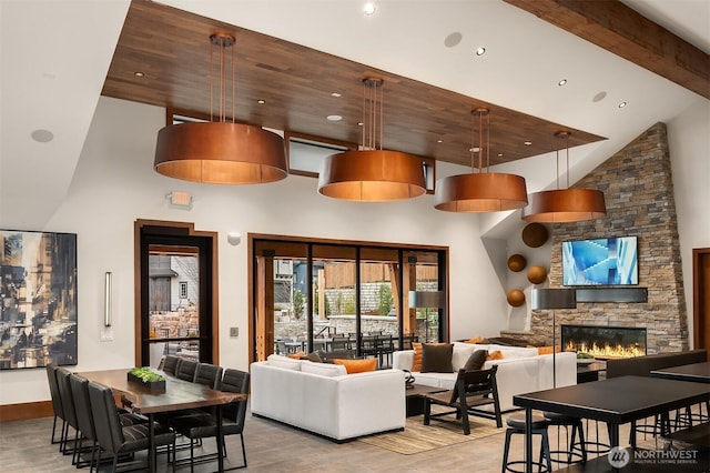 living room featuring light wood-type flooring, beamed ceiling, high vaulted ceiling, recessed lighting, and a stone fireplace