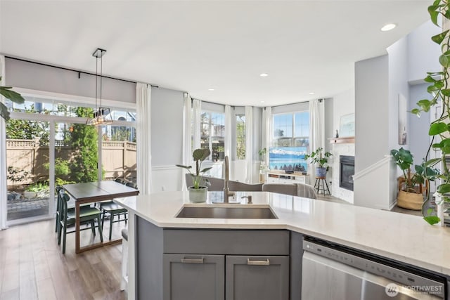 kitchen with stainless steel dishwasher, light countertops, a sink, and gray cabinets