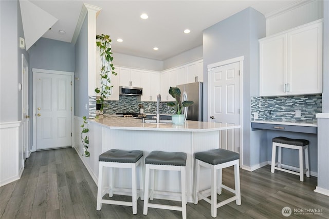 kitchen with backsplash, appliances with stainless steel finishes, a kitchen breakfast bar, and white cabinets