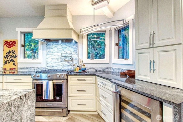 kitchen with stainless steel range with gas cooktop, dark stone counters, custom range hood, backsplash, and beverage cooler