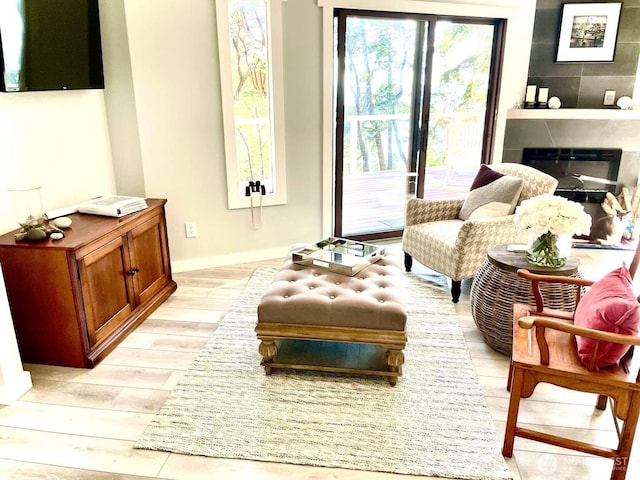 living area with light wood-type flooring, baseboards, and a glass covered fireplace