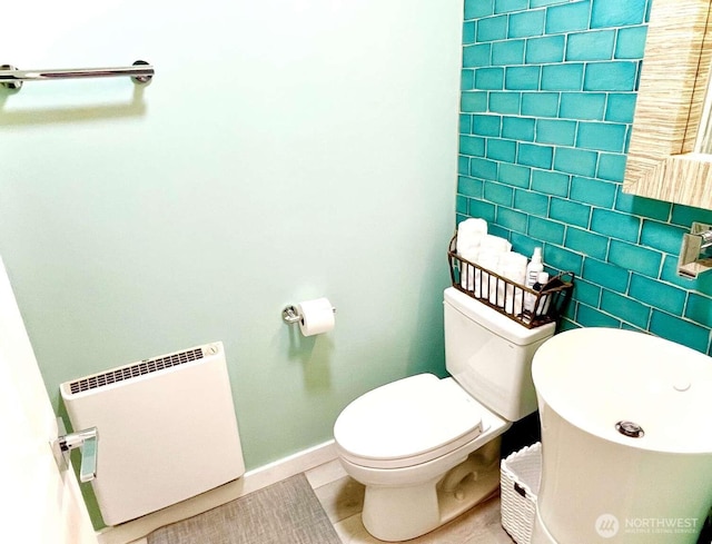 half bath with baseboards, tile patterned floors, toilet, radiator heating unit, and tile walls
