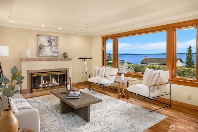 living room with crown molding, a tray ceiling, a glass covered fireplace, recessed lighting, and wood finished floors