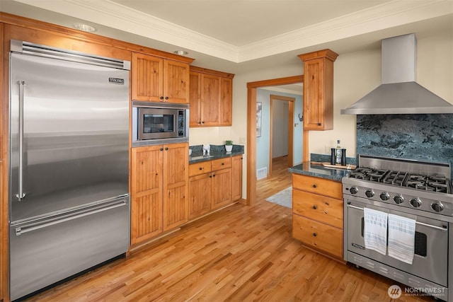 kitchen featuring crown molding, wall chimney exhaust hood, light wood-type flooring, built in appliances, and backsplash