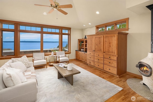 living area with a water view, a wood stove, light wood-type flooring, a ceiling fan, and recessed lighting