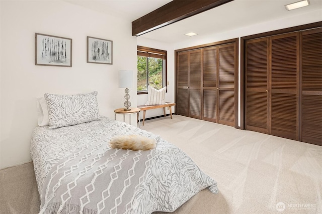 carpeted bedroom with beam ceiling and multiple closets