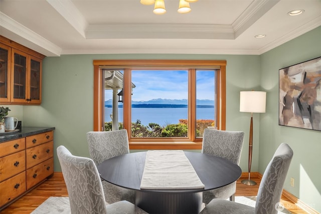 dining area with a water and mountain view, wood finished floors, ornamental molding, and a raised ceiling