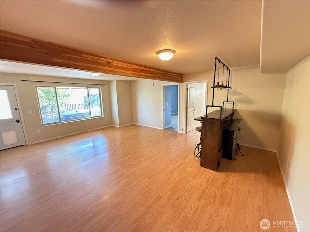 unfurnished living room featuring baseboards, a textured ceiling, light wood-type flooring, and beam ceiling