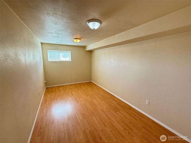 empty room with baseboards, a textured ceiling, a textured wall, and wood finished floors