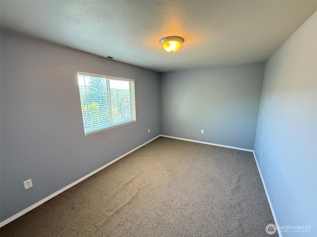 spare room with carpet floors, a textured ceiling, baseboards, and visible vents