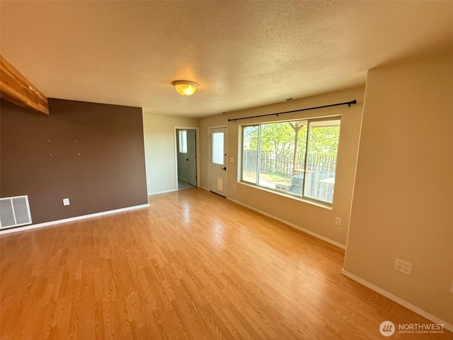 unfurnished room featuring visible vents, a textured ceiling, baseboards, and light wood finished floors